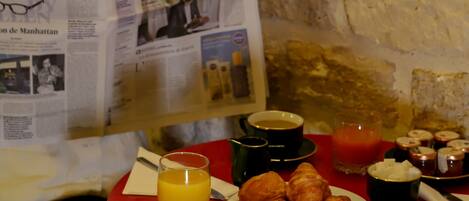 A breakfast table with croissants, juice, coffee, and jam. A newspaper titled "LE FIGARO" is being read.
