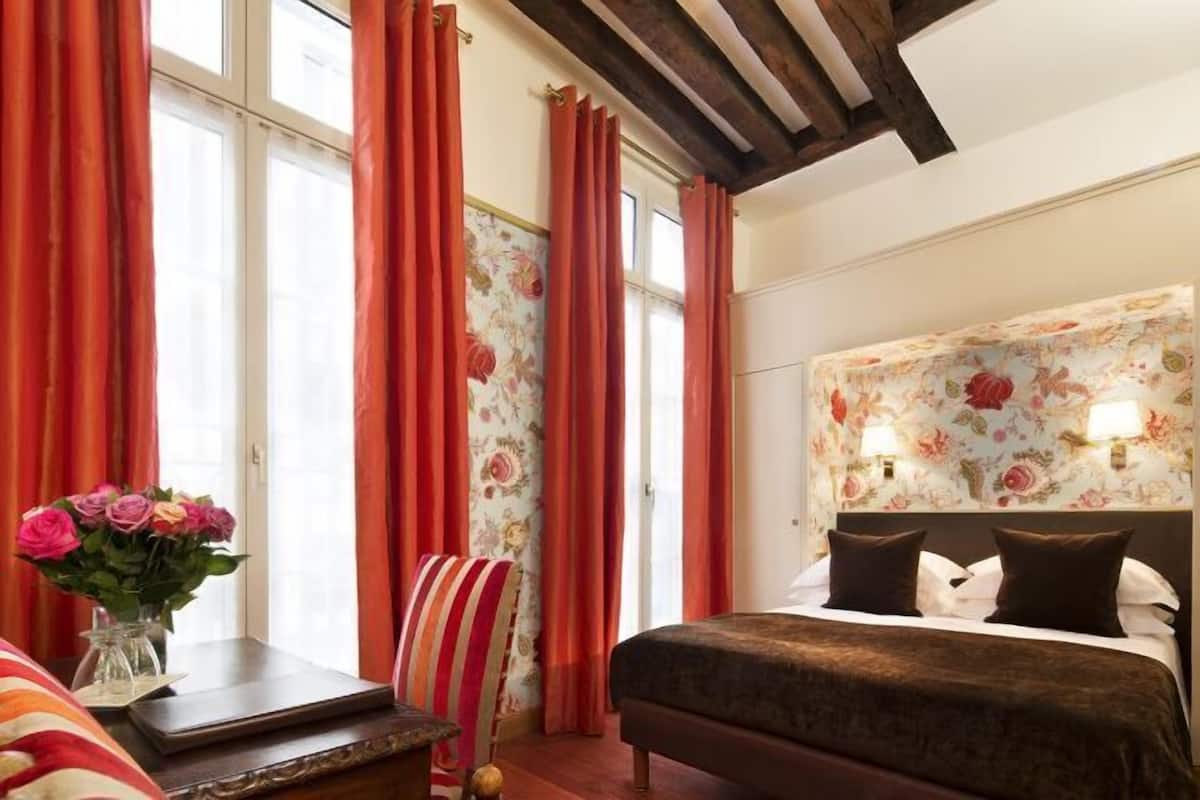 Ein Hotelzimmer mit Bett, Stuhl, Schreibtisch und einem fenster mit Vorhängen.