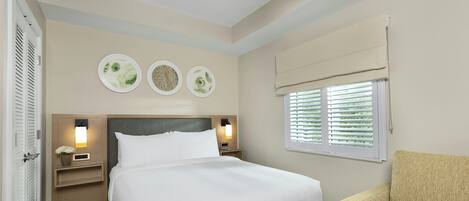 A hotel room with a bed, bedside tables, a ceiling fan, a window with blinds, and a chair.