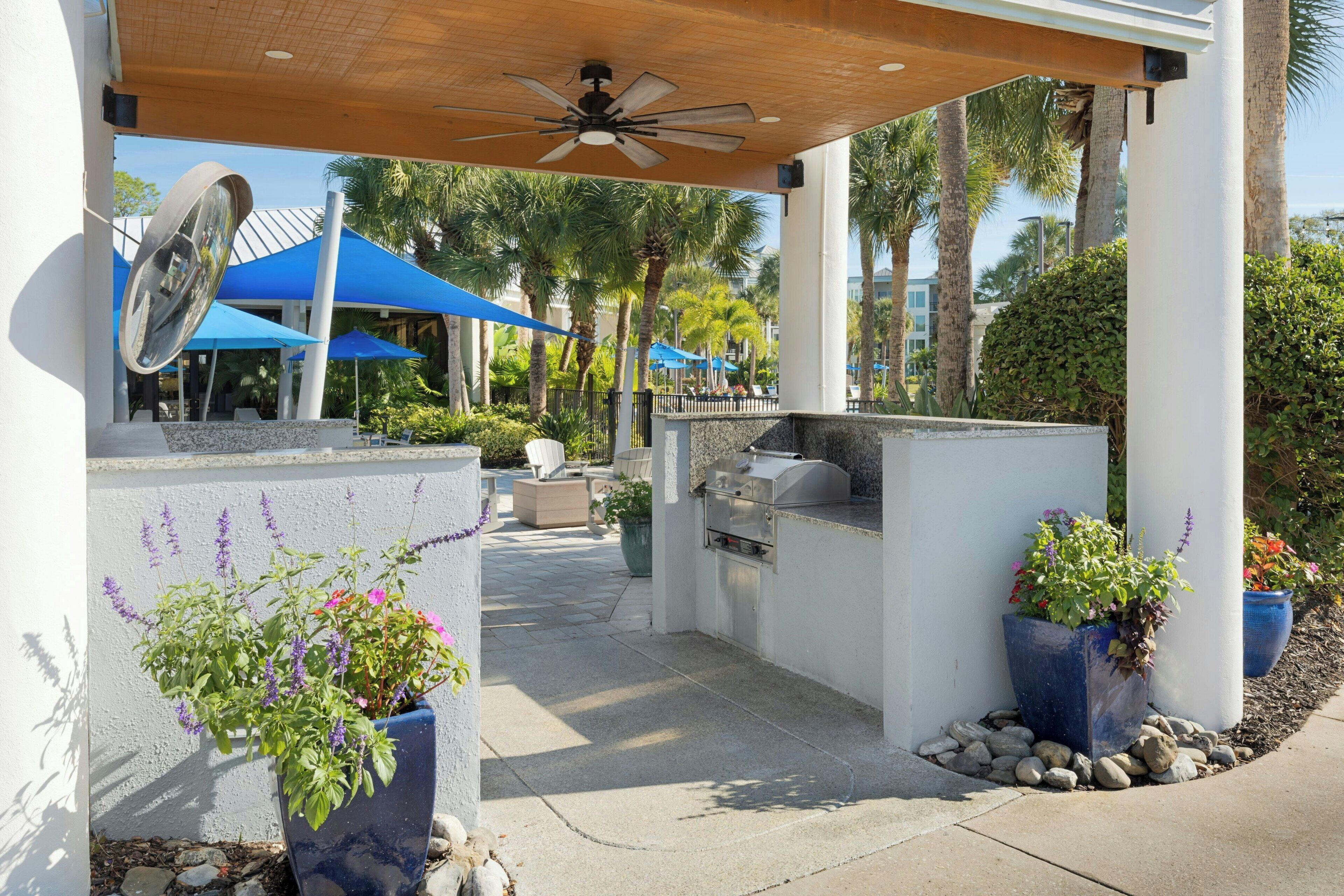 An outdoor patio area with a ceiling fan, grilling station, and potted plants.