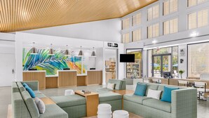 A modern hotel lobby with green sofas, a reception desk, a large TV screen, and a wooden ceiling. - Marriott's Royal Palms (Orlando)