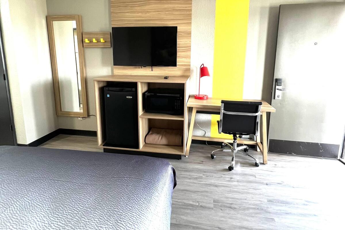 A hotel room with a bed, a desk with a computer, a television, a microwave, and a red lamp.