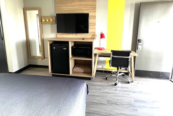 A hotel room with a bed, a desk with a computer, a television, a microwave, and a red lamp. - Super 8 by Wyndham Manchester TN (Manchester)
