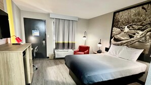 A hotel room with a bed, a desk, a chair, a TV, a window with curtains, and a wall-mounted picture. - Super 8 by Wyndham Manchester TN (Manchester)