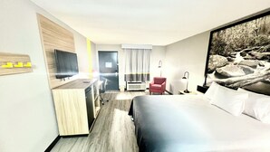 A hotel room with a bed, desk, chair, TV, air conditioning unit, and a painting on the wall. - Super 8 by Wyndham Manchester TN (Manchester)