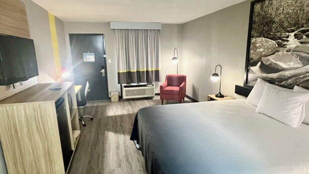 A hotel room with a bed, a desk with a chair, a TV, a red armchair, a lamp, and a painting on the wall. - Super 8 by Wyndham Manchester TN (Manchester)