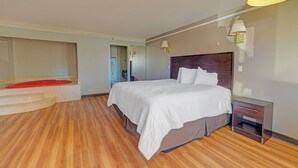 A hotel room with a large bed, wooden flooring, a nightstand, and a red chair. - Travelers inn by OYO Wichita Falls (Wichita Falls)