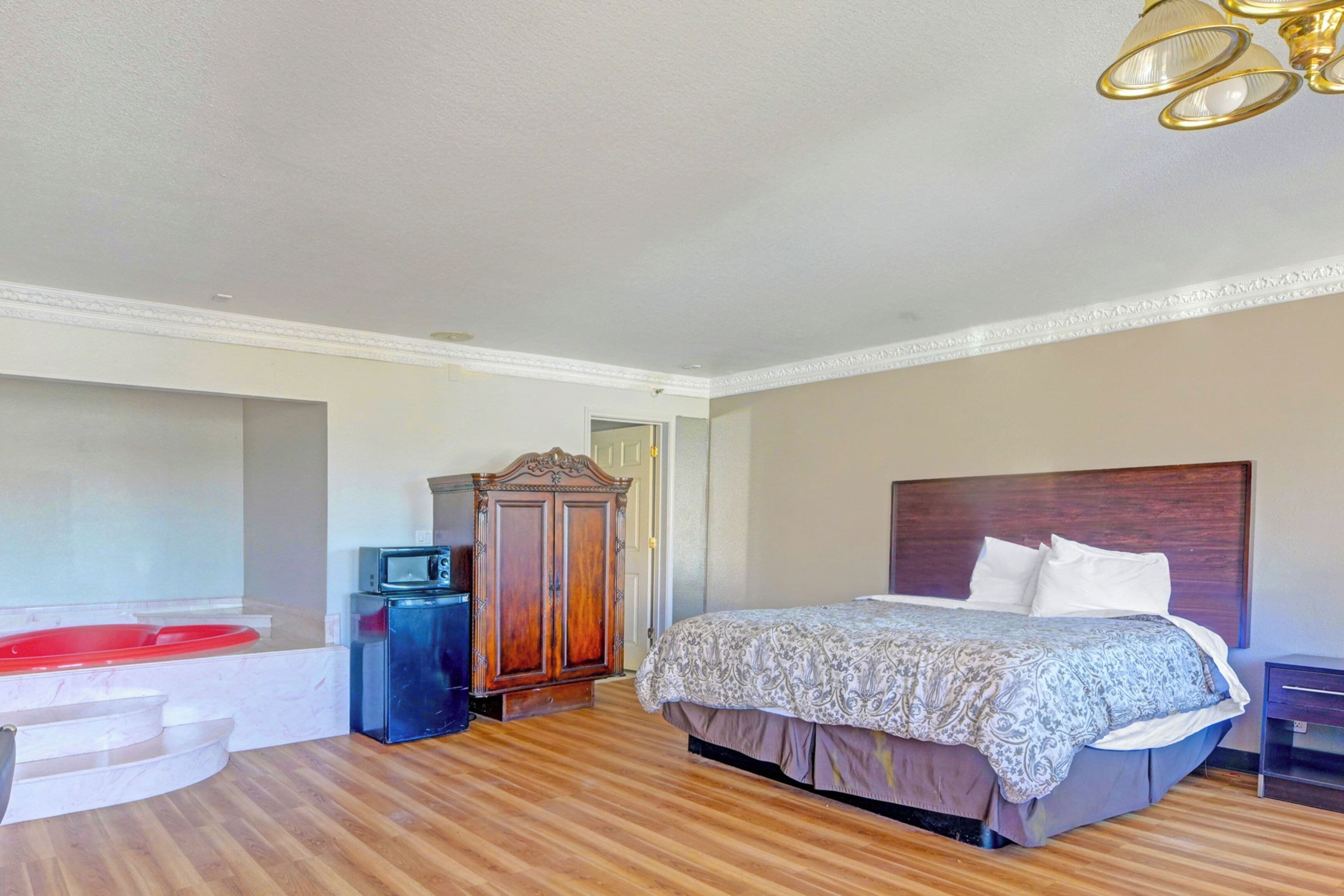 A bedroom with a bed, a wooden wardrobe, a red bathtub, and a small TV.