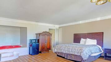 A bedroom with a bed, a wooden wardrobe, a red bathtub, and a small TV.