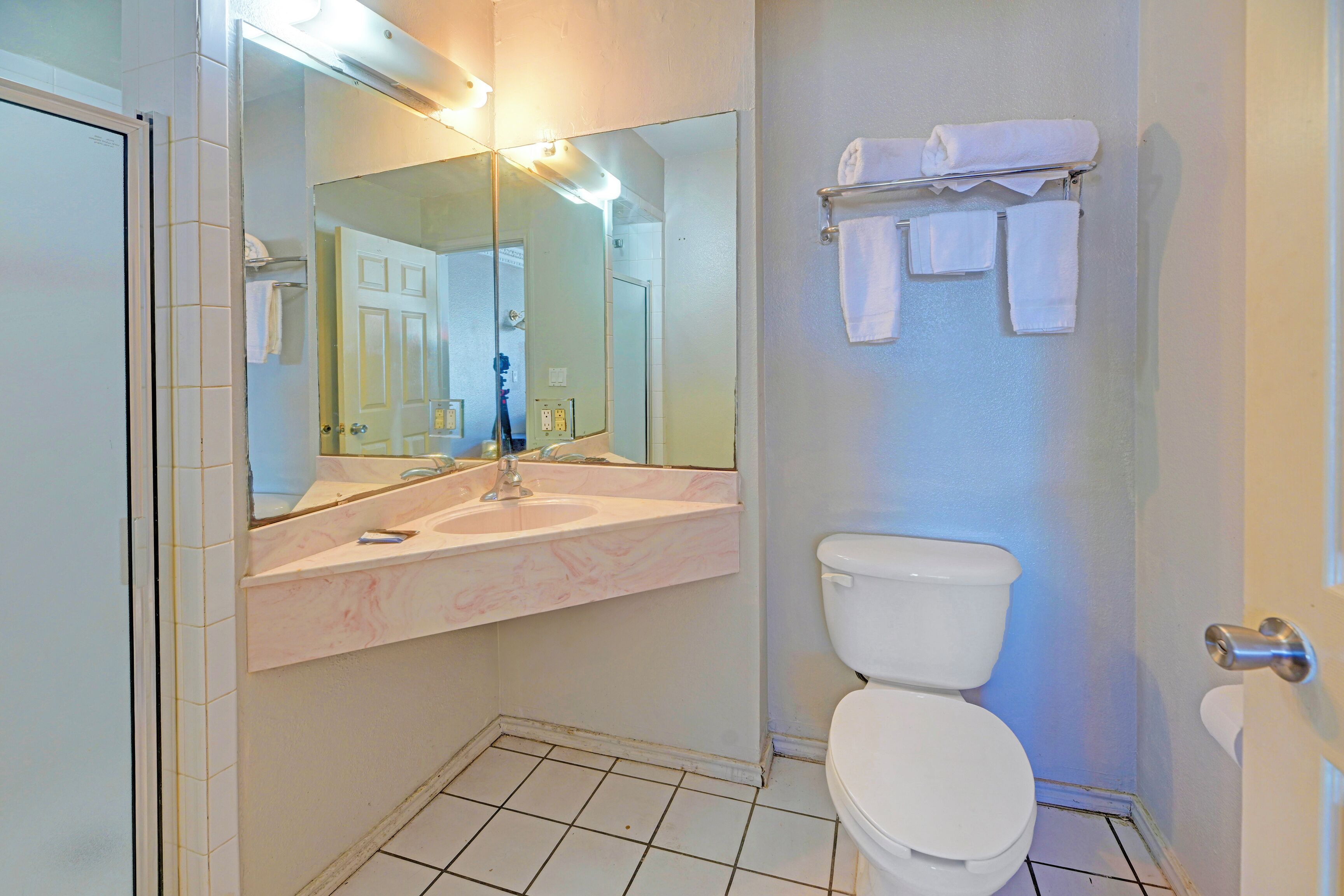 A bathroom with a white toilet, a sink with a marble countertop, a large mirror, and a towel rack with several towels.