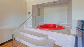A bathroom with a red bathtub, marble steps, and a stainless steel shower. - Travelers inn by OYO Wichita Falls (Wichita Falls)