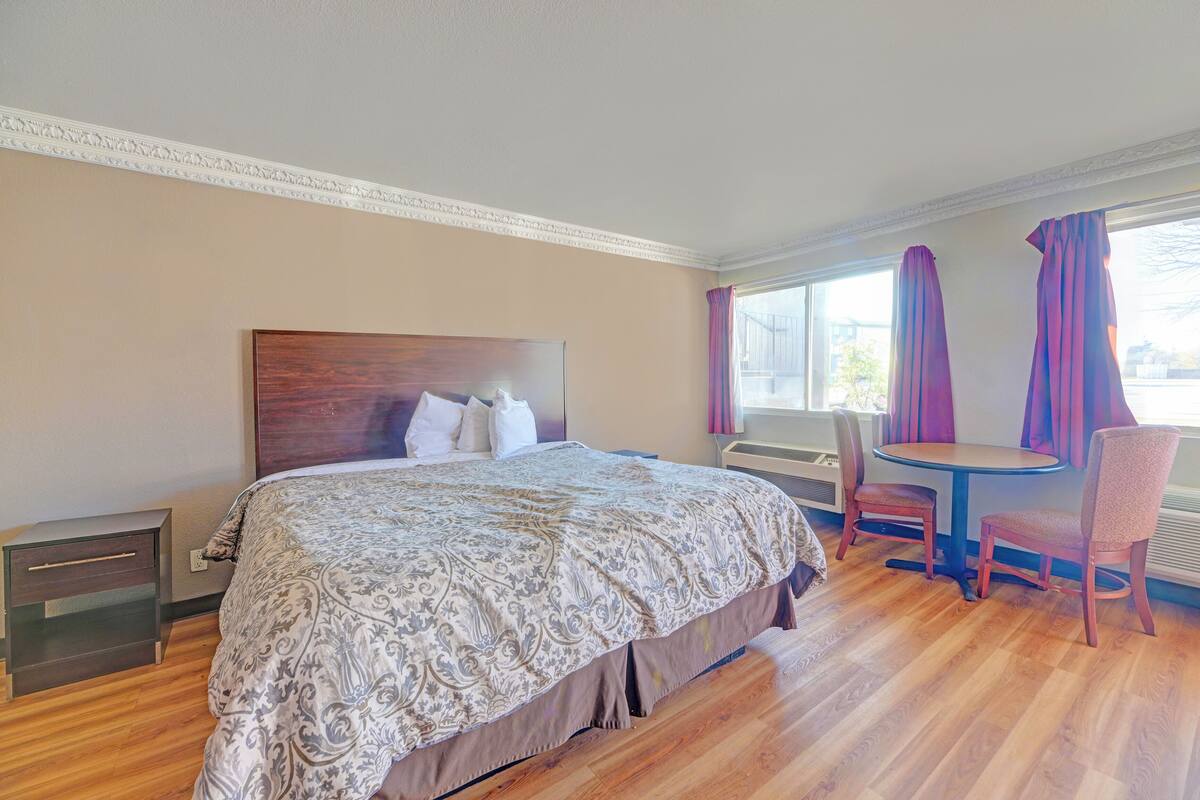 A hotel room with a large bed, a small table with two chairs, a window with curtains, and a decorative ceiling molding.