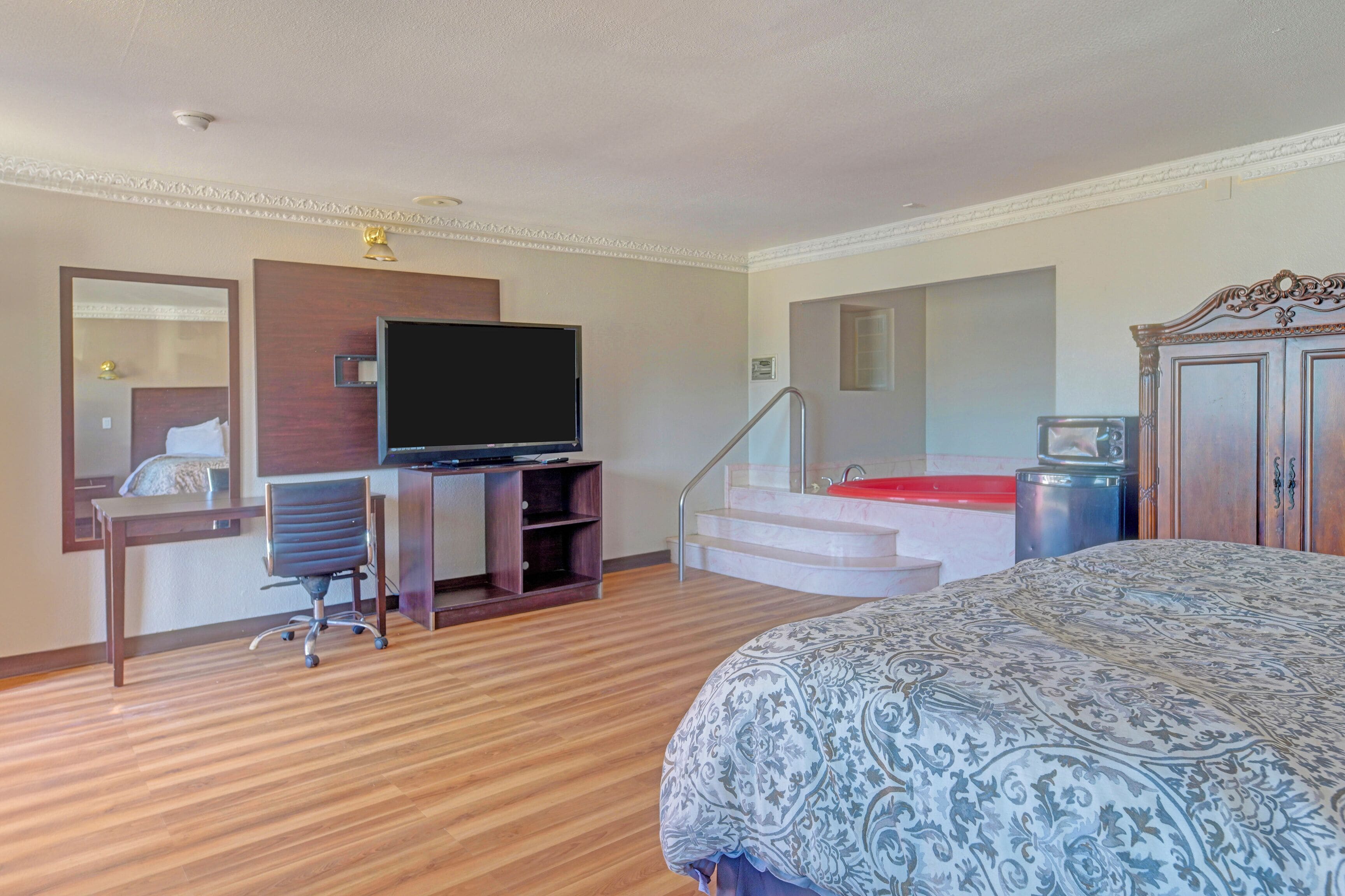Quarto de hotel com cama, escrivaninha com computador, televisão e escada.