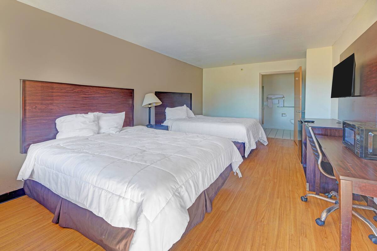A hotel room with two beds, a desk, a TV, and a bathroom visible through an open door.