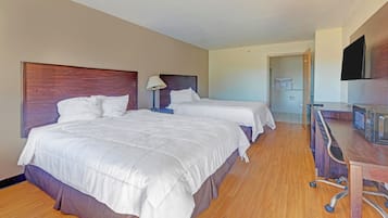 Habitación de hotel con dos camas, un escritorio, televisor y baño visible a través de una puerta abierta.
