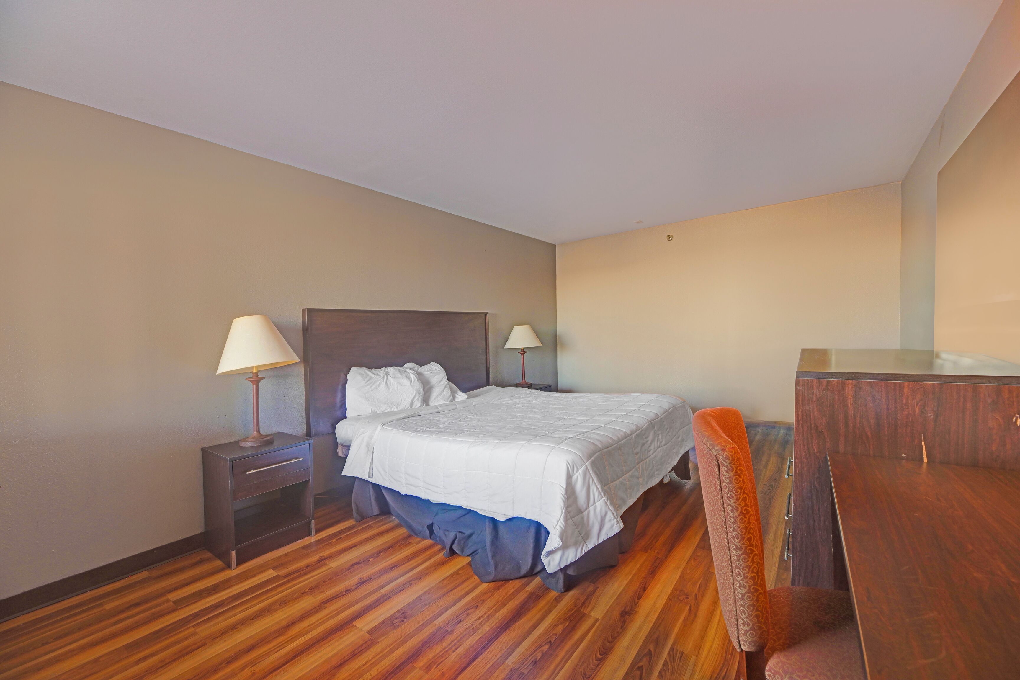 A hotel room with a wooden floor, a bed with white bedding, two bedside tables with lamps, and a wooden desk.