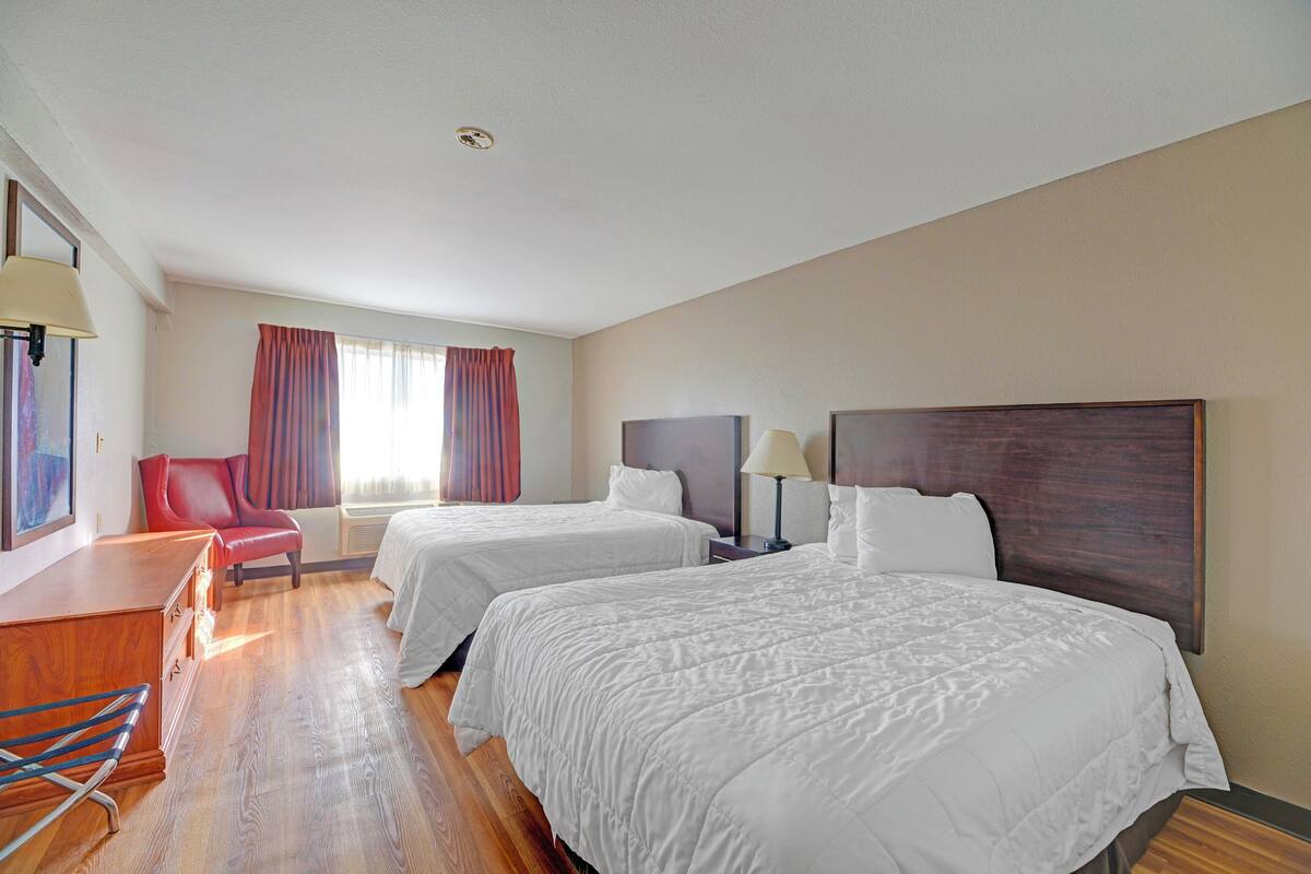 A hotel room with two beds, a desk, a chair, and a window with curtains.