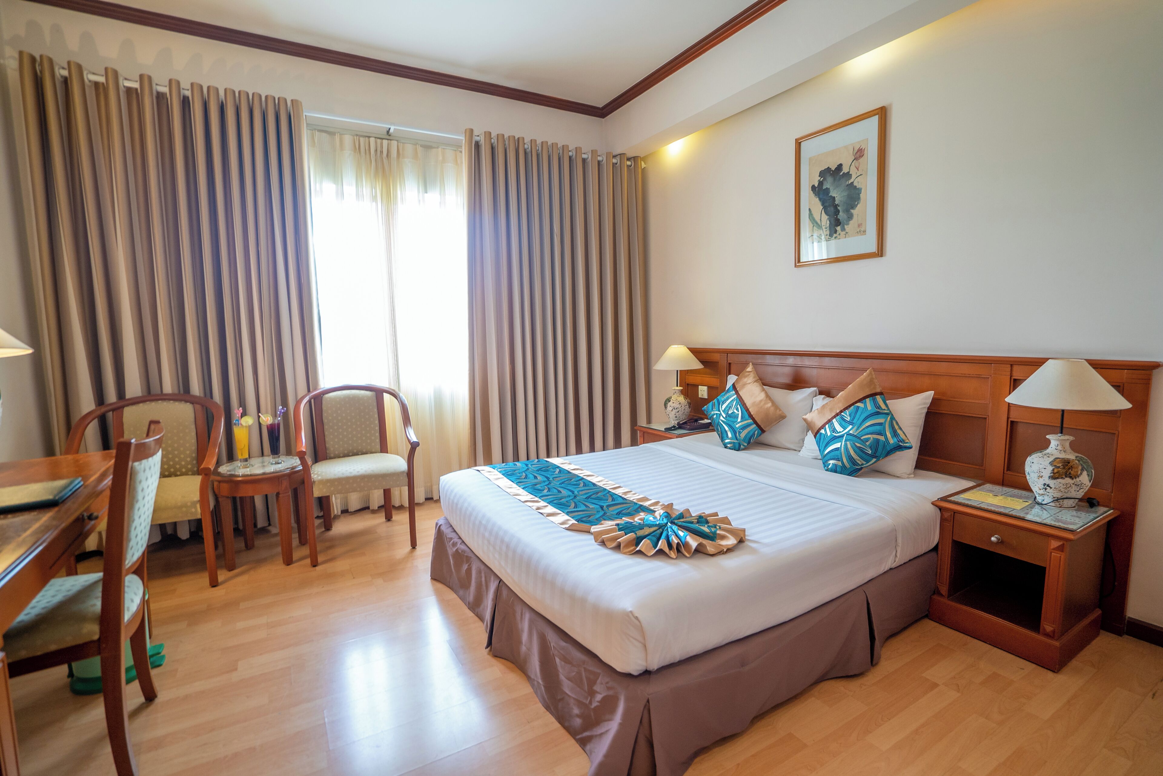A hotel room with a large bed, two chairs, a desk, and a nightstand with a lamp.