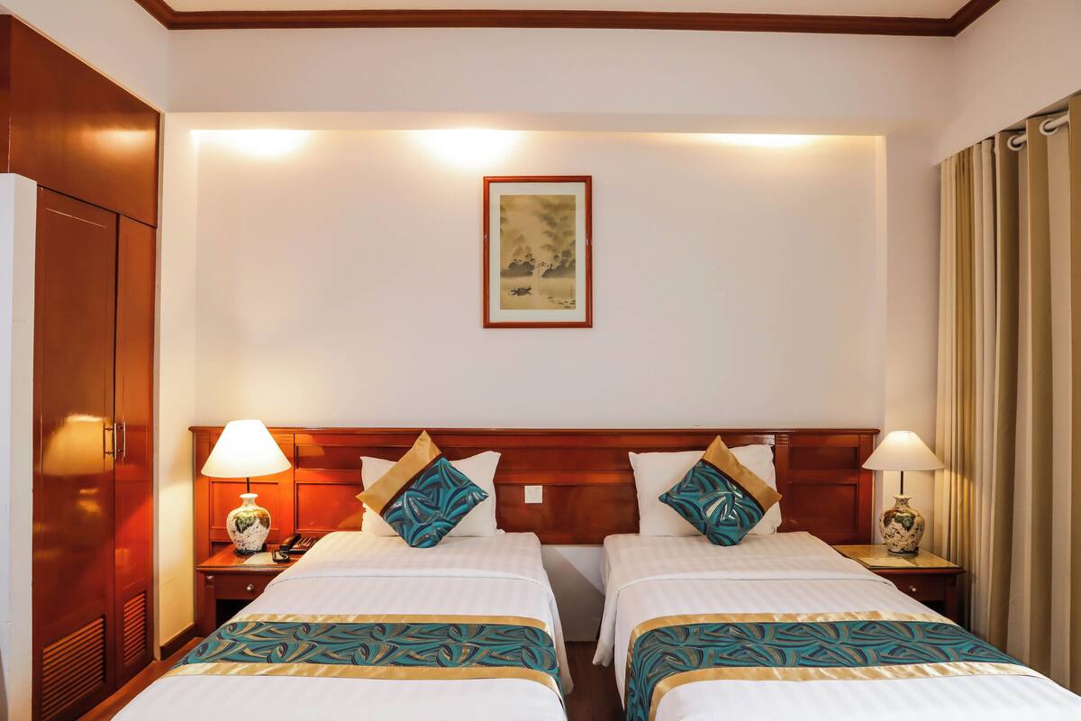 Ein Hotelzimmer mit zwei Betten, einem Holzkopfteil, Nachttischlampen und einem gerahmten Kunstwerk an der Wand.