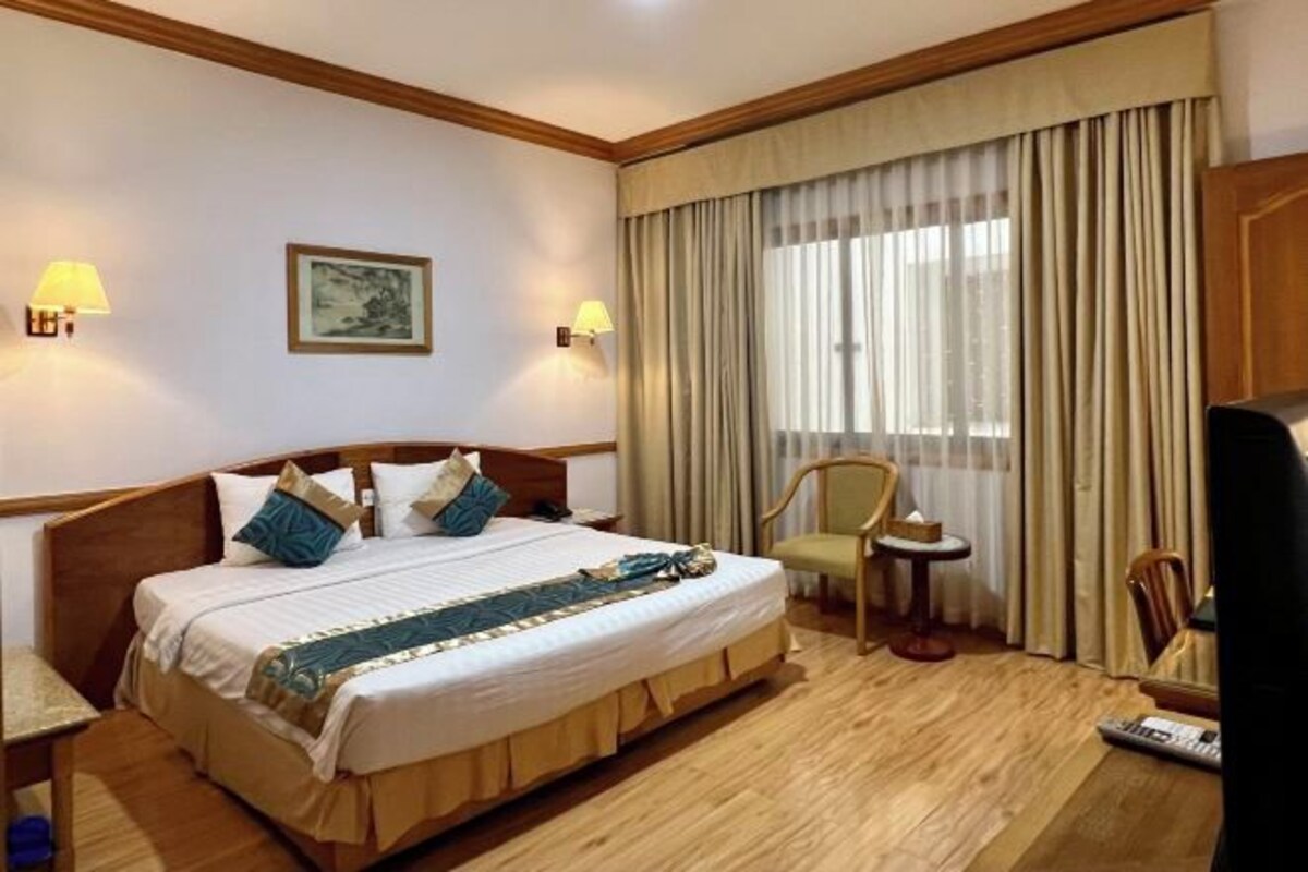 Une chambre d’hôtel avec un grand lit, deux lampes de chevet, une petite table, une chaise et un téléviseur.