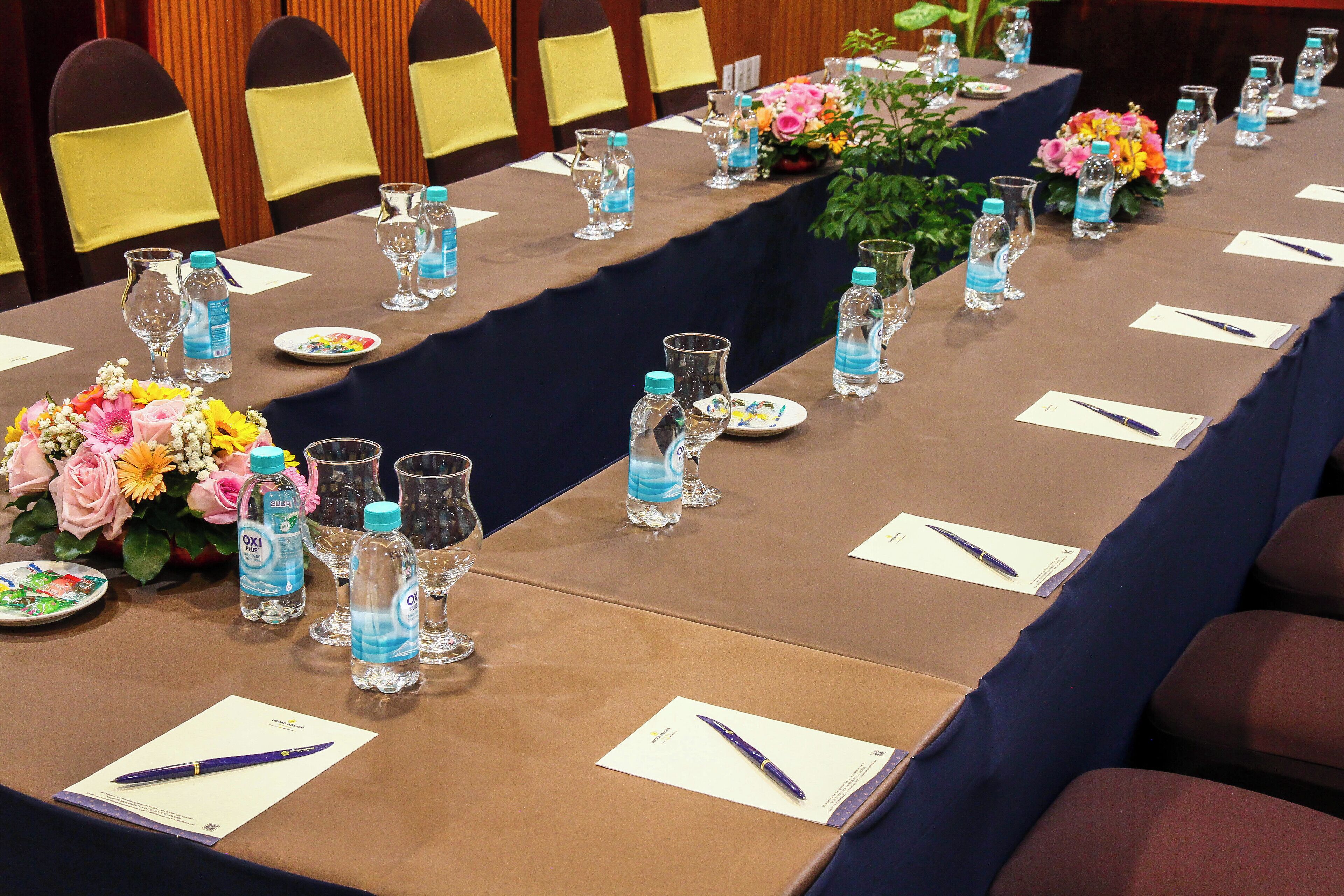 A conference table set with water bottles, glasses, and plates, surrounded by chairs.
