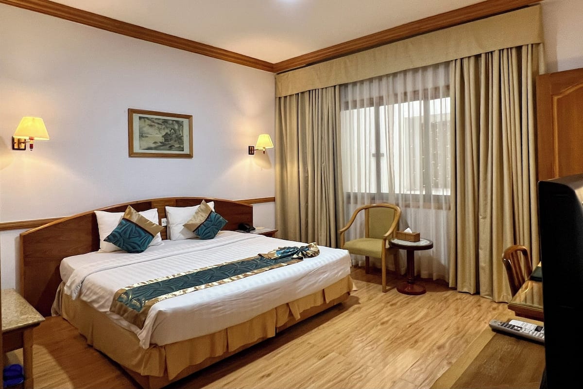 Hotelkamer met een groot bed, twee bedlampen, een klein tafeltje, een stoel, een televisie en een raam met gordijnen.