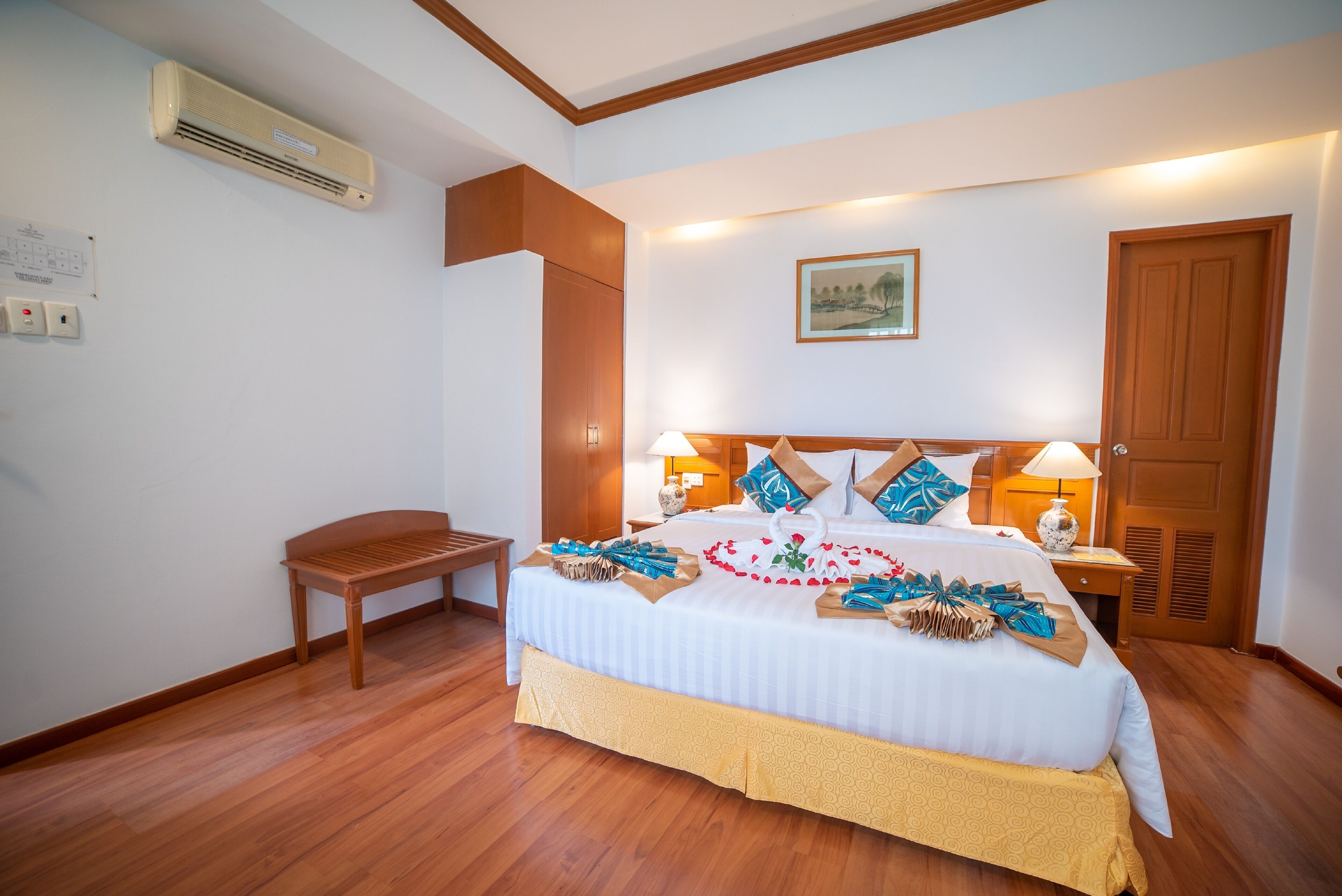 A neatly arranged bedroom with a wooden bench, a bed with decorative pillows, and a bedside table with a lamp.