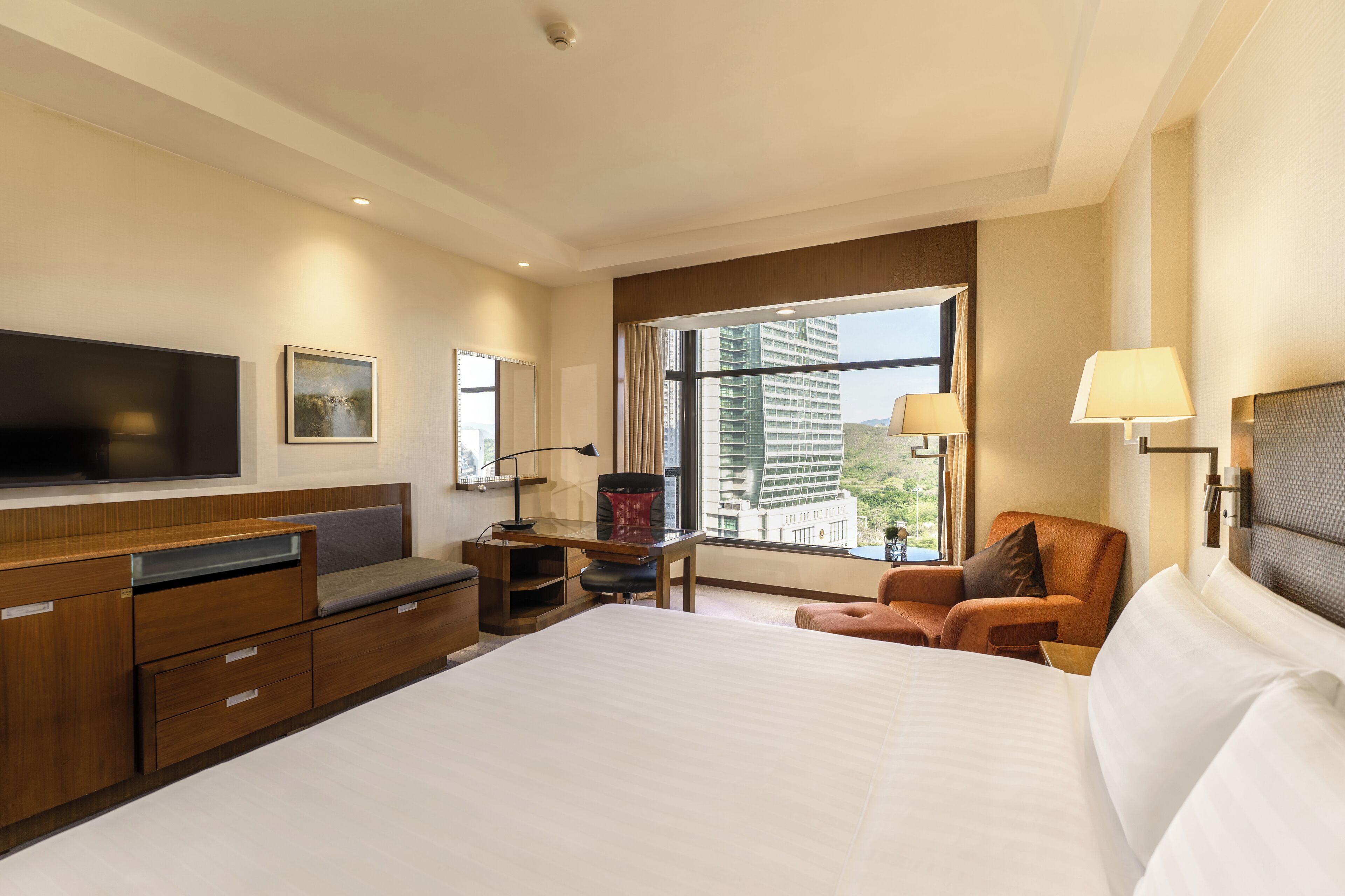 Een hotelkamer met een groot bed, een bureau met stoel, een televisie en een raam met uitzicht op de stad.