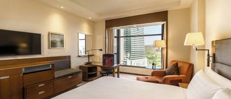 A hotel room with a large bed, a desk with a chair, a TV, and a window with a city view.