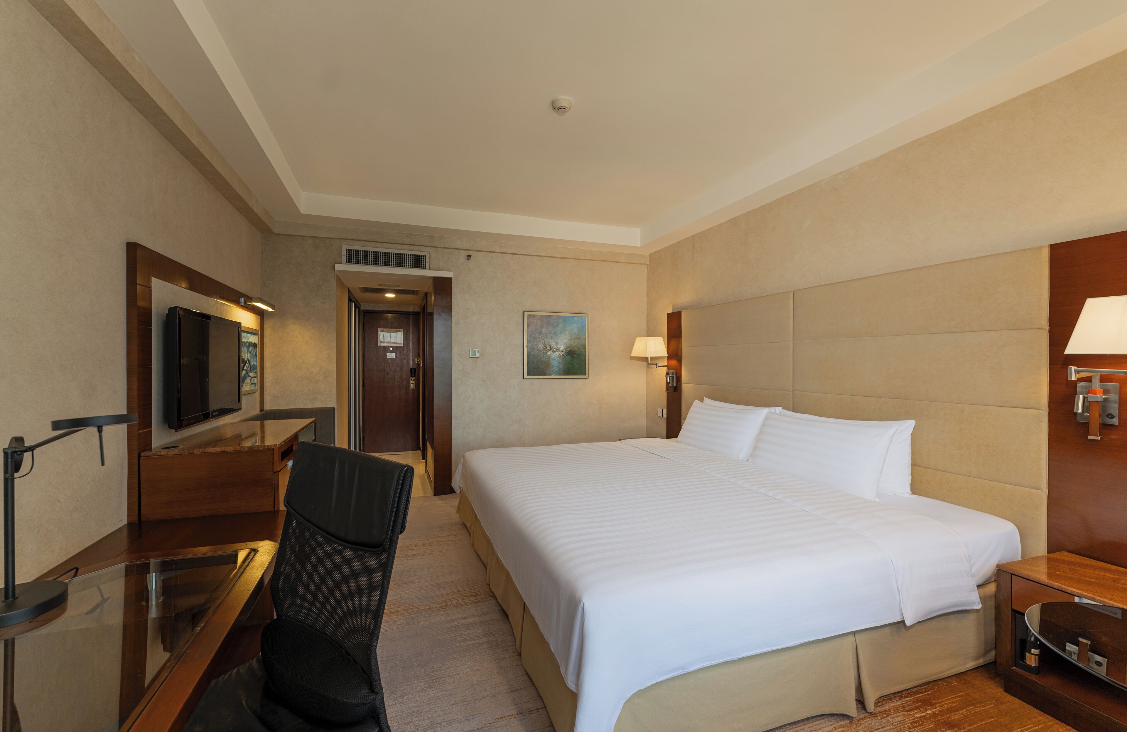 A hotel room with a large bed, a desk with a chair, a television, and a painting on the wall.