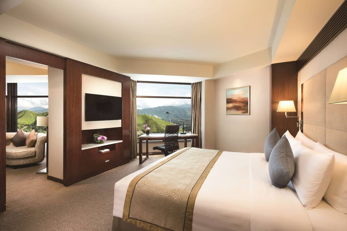 A hotel room with a large bed, a desk, a TV, and a view of mountains.