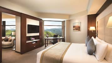 A hotel room with a large bed, a desk, a TV, and a view of mountains.