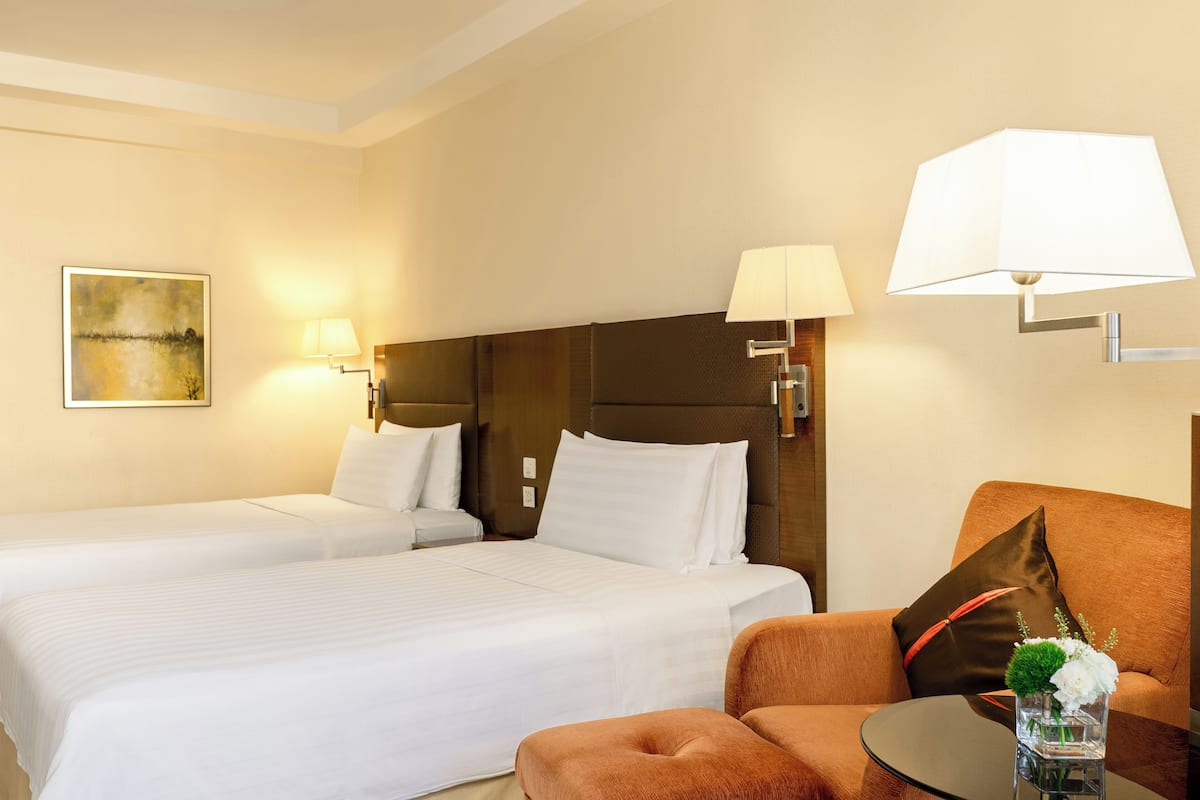 A hotel room with two beds, a sofa, a small table, and a lamp.