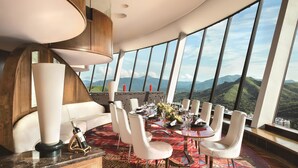 A dining area with a panoramic mountain view, a modern chandelier, and a patterned carpet. - Shangri-La Shenzhen (Shenzhen)