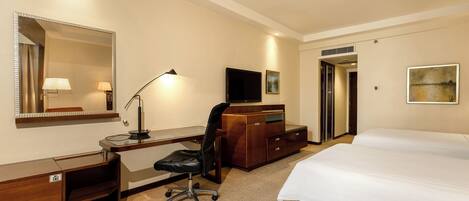 A hotel room with a bed, a desk with a chair, a television, a mirror, and a door.