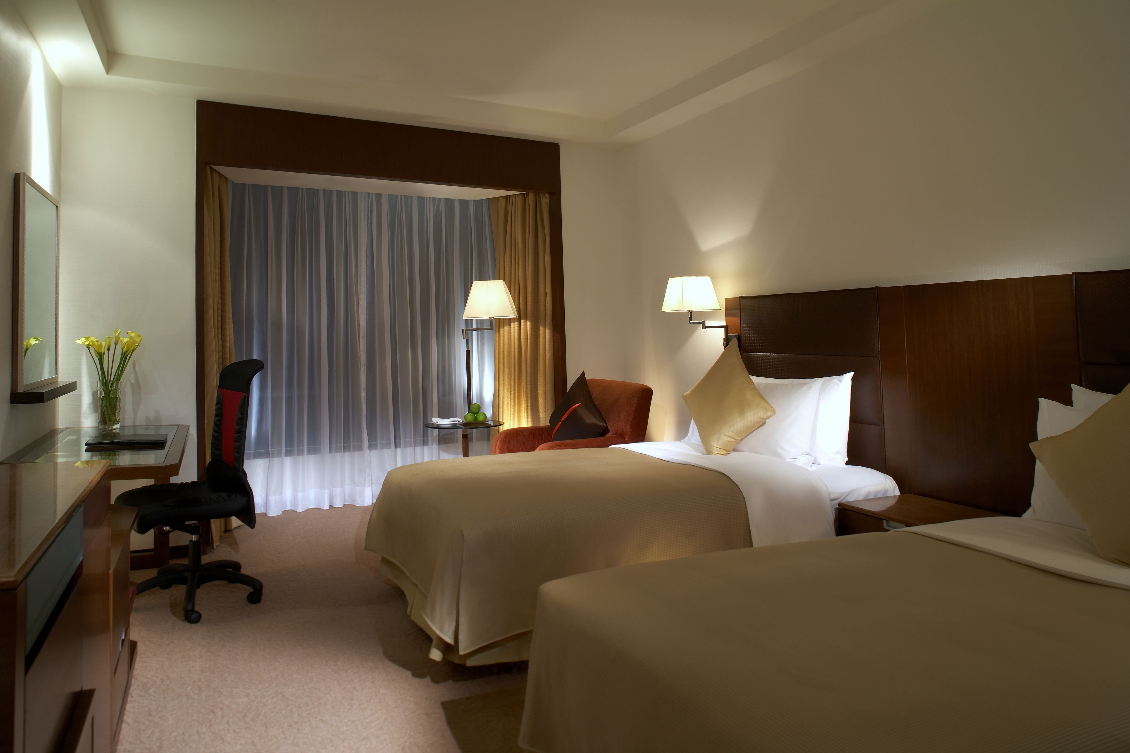 Een hotelkamer met twee bedden, een bureau, een stoel en een lamp.