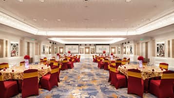 Un salón de banquetes con mesas redondas, sillas rojas y una alfombra estampada.