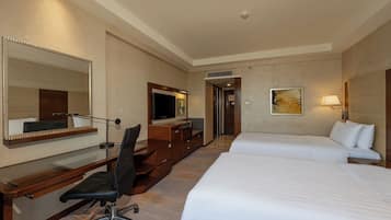 A hotel room with a desk, chair, two beds, a TV, and a painting.