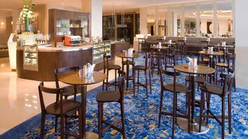 Eine Hotelhalle mit einer zentralen Bar, verschiedenen Sitzgelegenheiten und einem gemusterten Teppich.