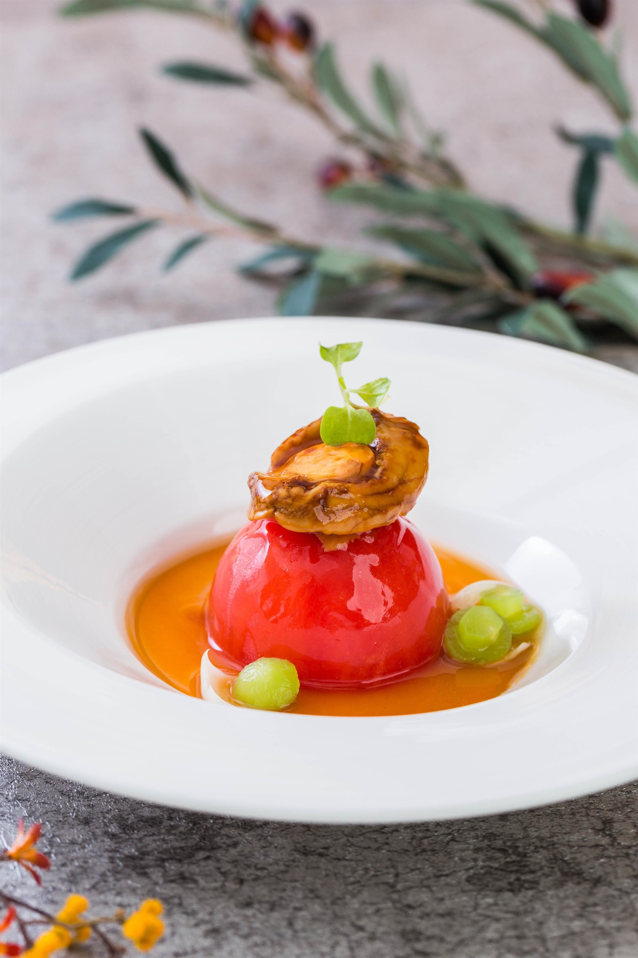 A white plate with a red spherical food item, green garnish, and a mushroom on top.