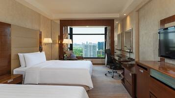 A hotel room with two beds, a desk, a chair, a television, and a large window offering a city view.