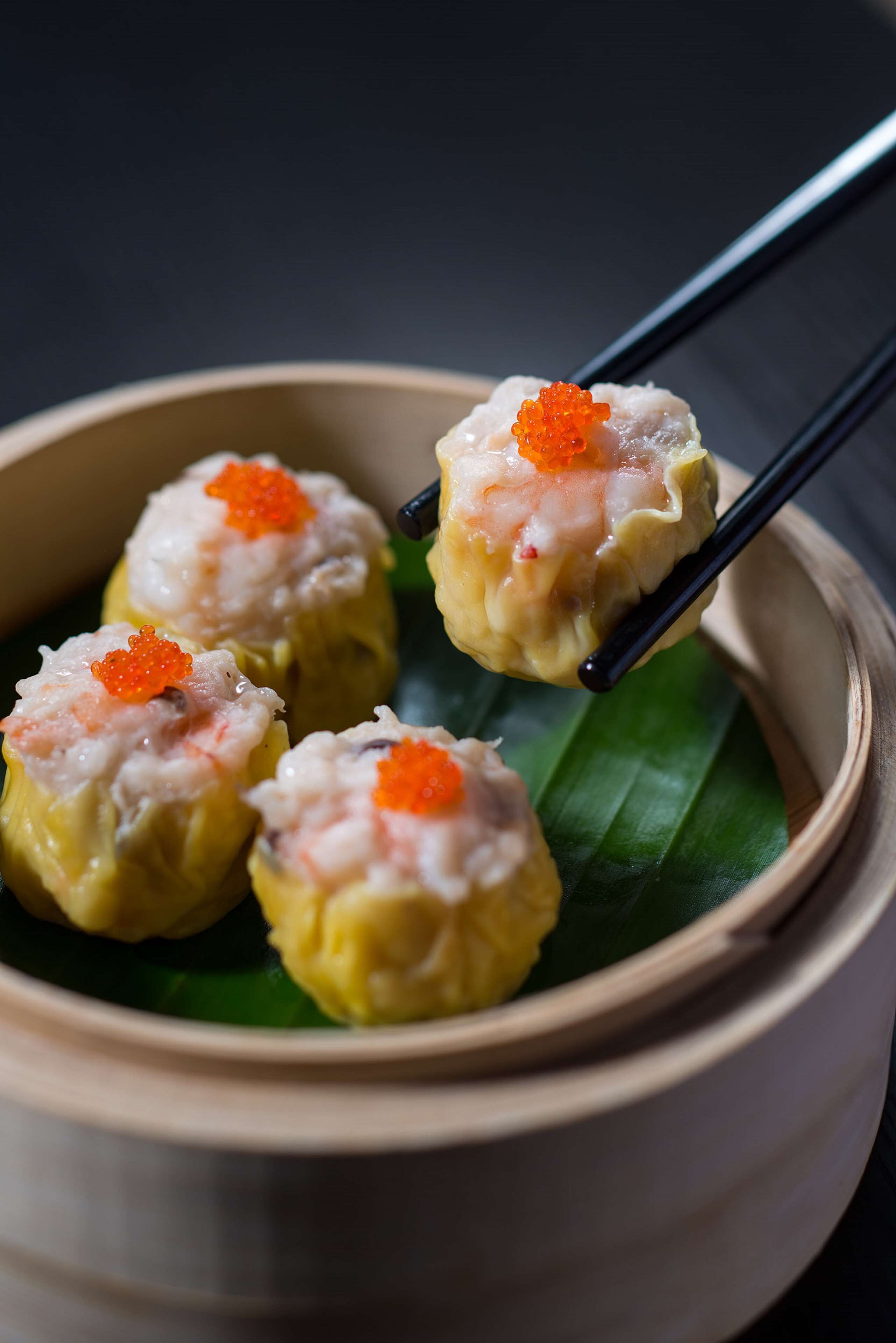 A bowl of dumplings with a red topping, held by chopsticks.
