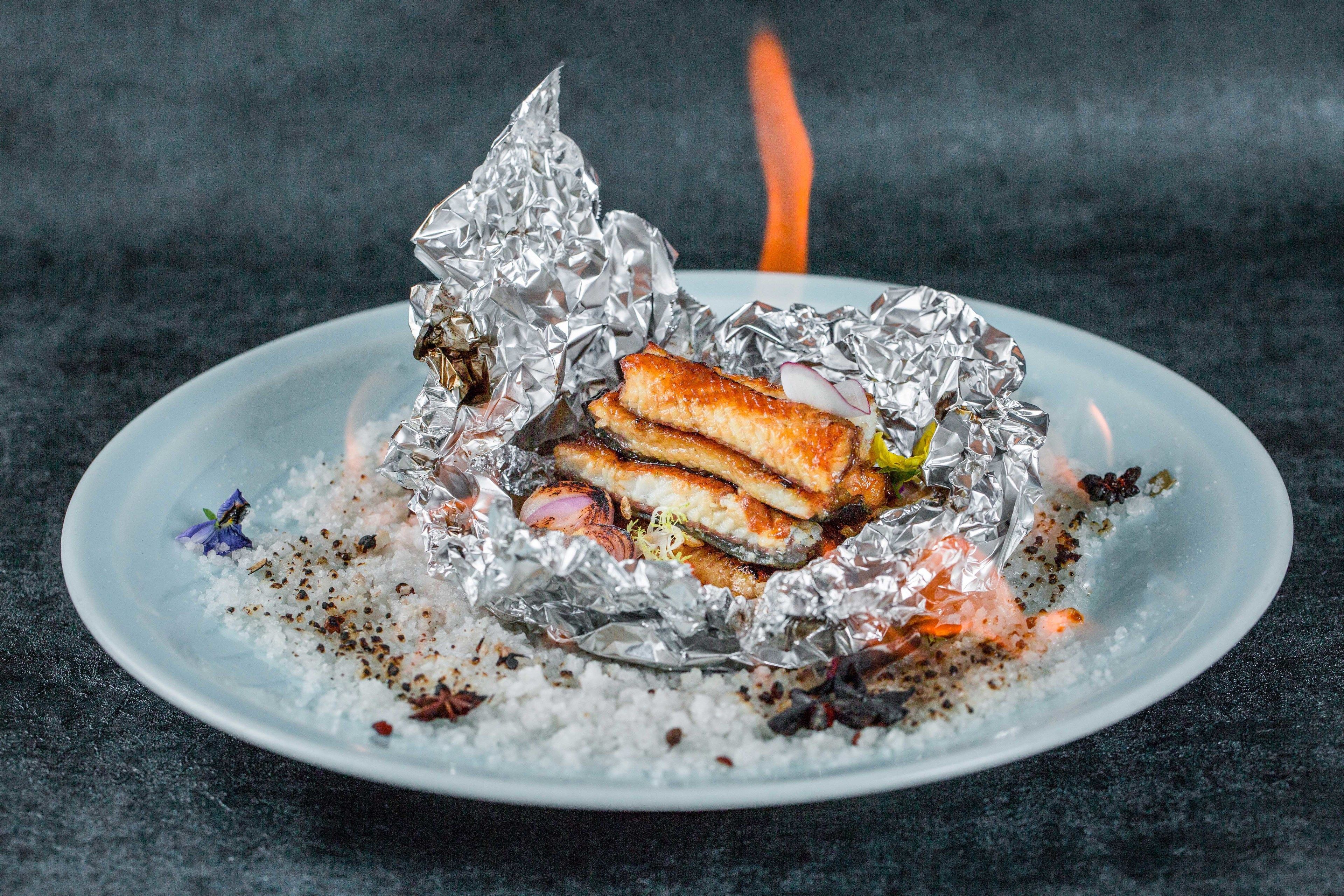 A plate with a grilled sandwich wrapped in foil, surrounded by scattered spices and herbs.
