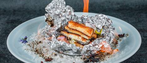 A plate with a grilled sandwich wrapped in foil, surrounded by scattered spices and herbs.