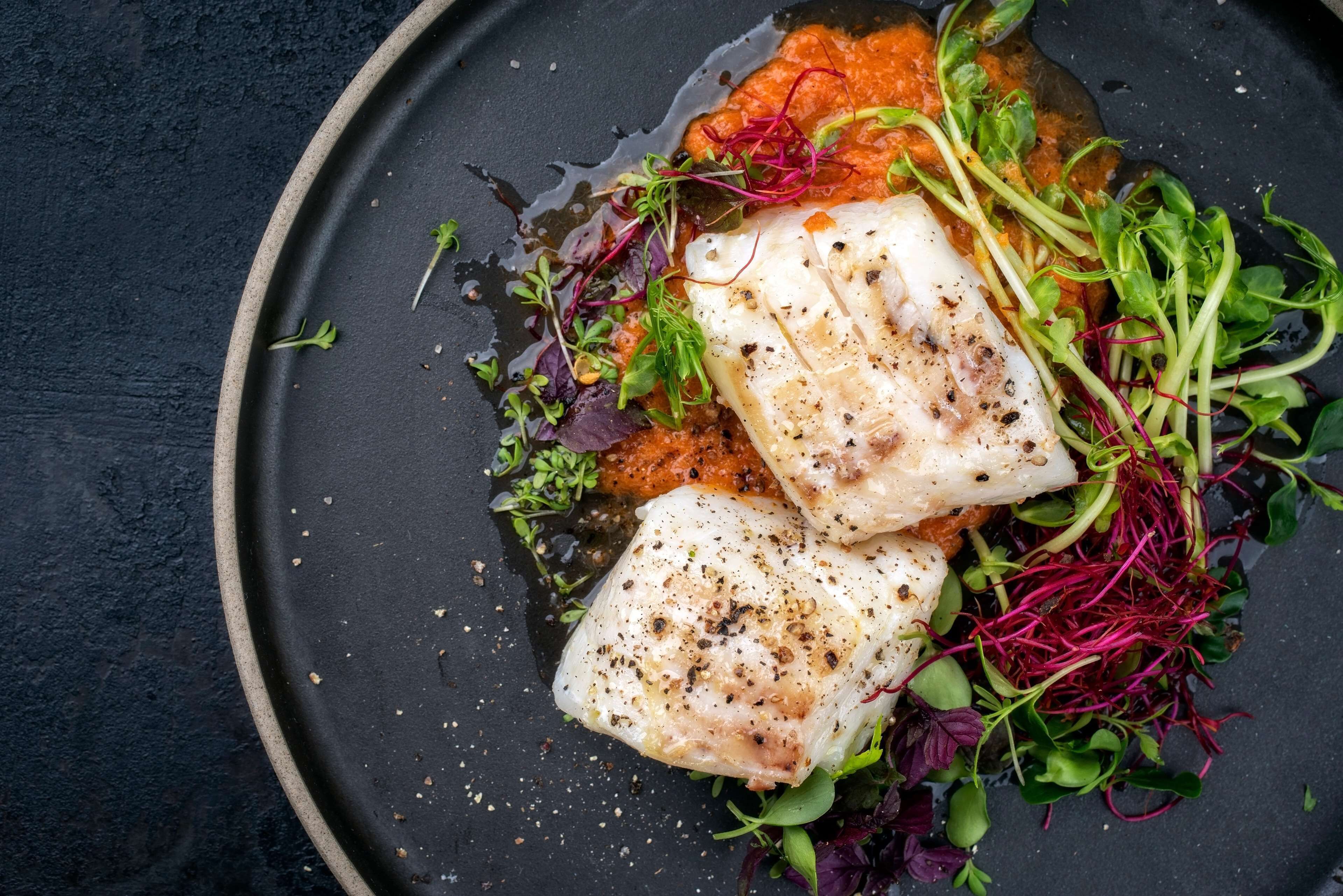 A plate with fish, greens, and a sauce.