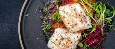 A plate with fish, greens, and a sauce.