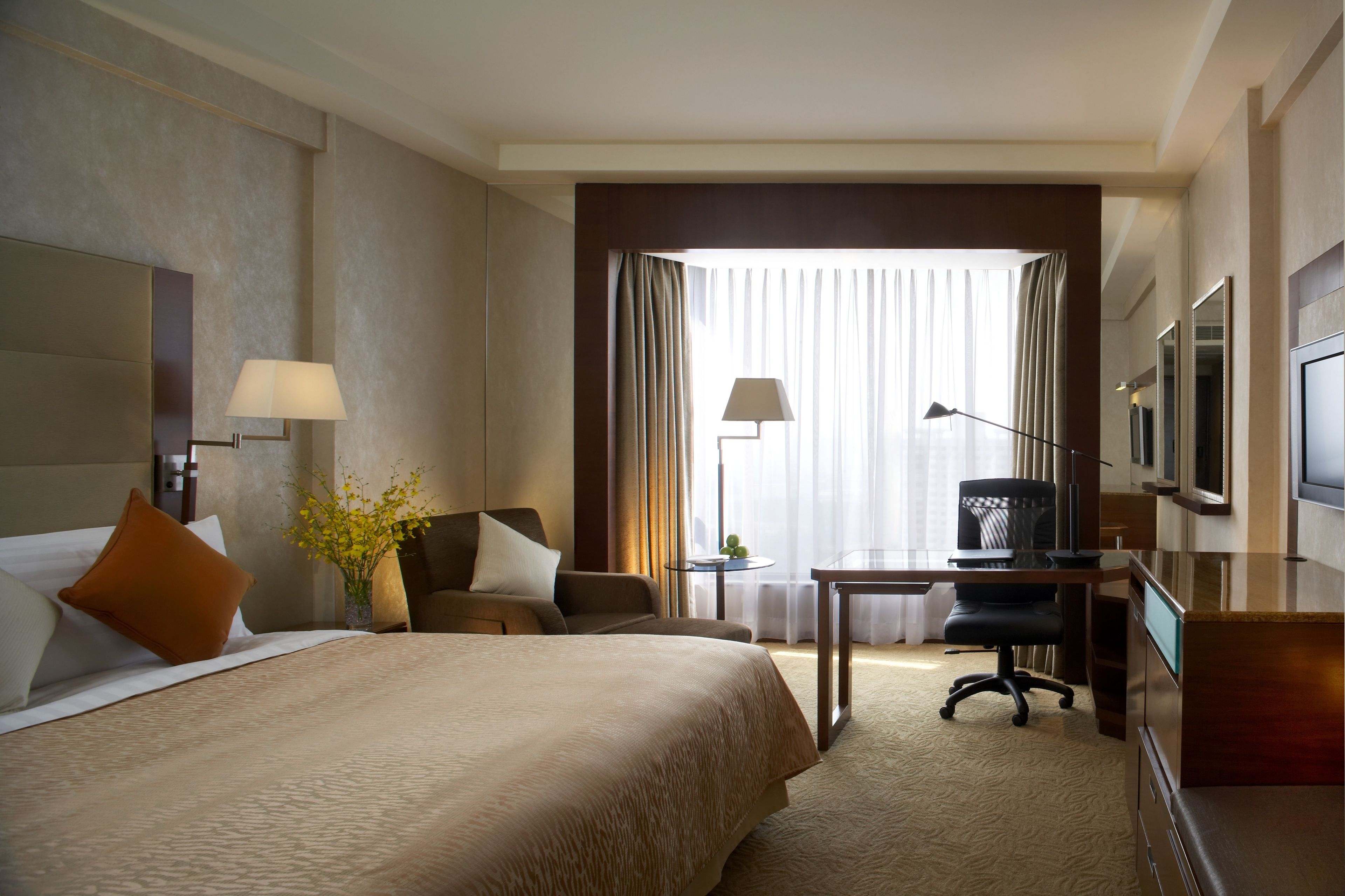 Habitación de hotel con una cama grande, un escritorio con silla, televisión y ventana con cortinas.