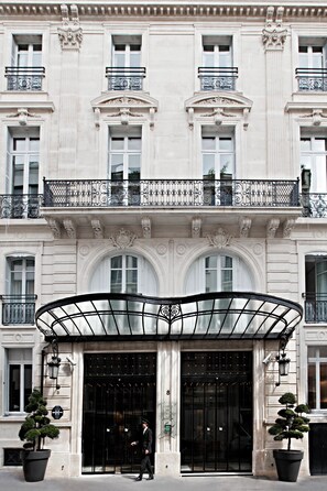 A classical building facade with ornate balconies, large arched windows, and a prominent entrance with a glass canopy. - La Maison Champs Elysées (Paris)