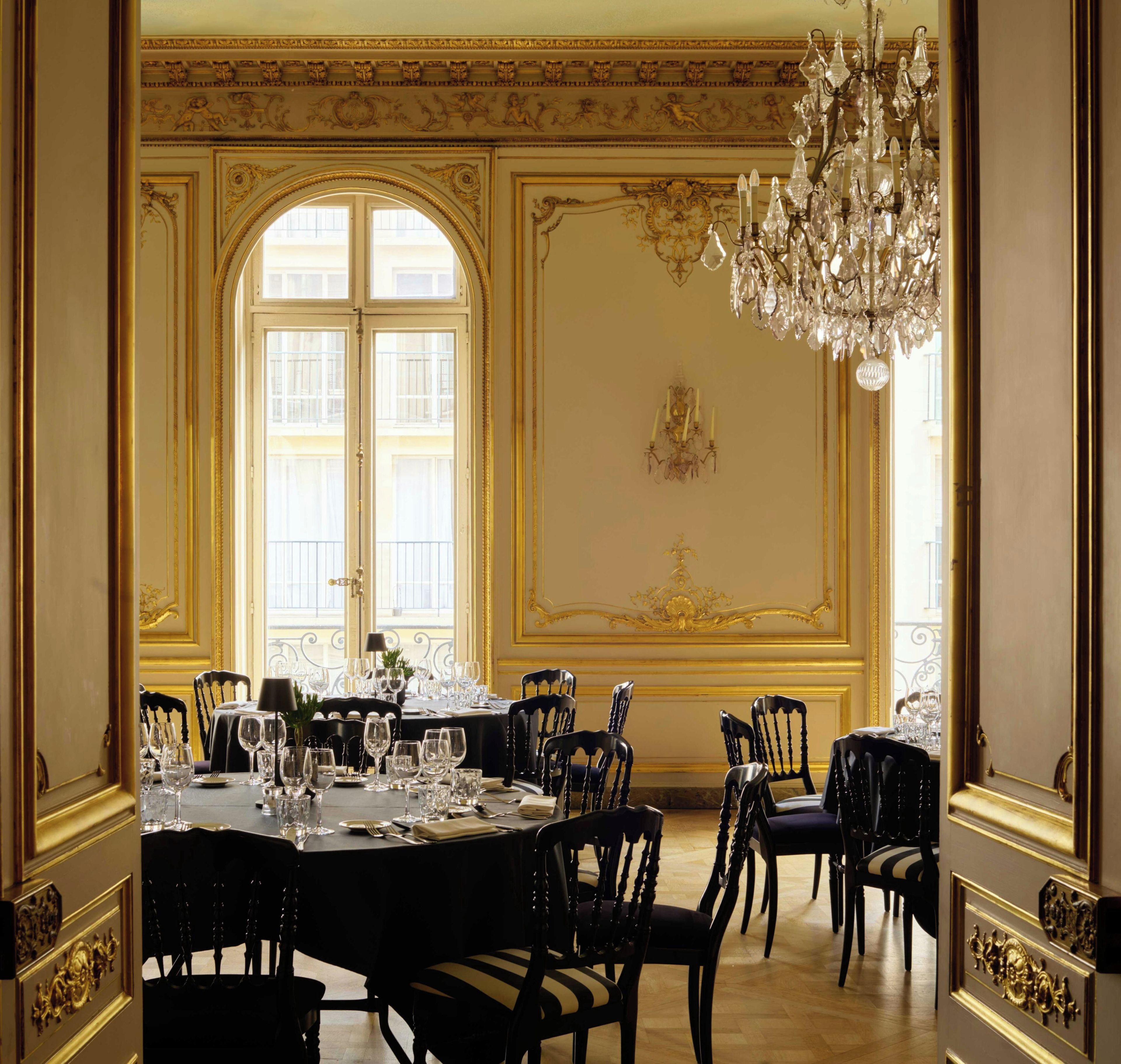 Ein formeller Speisesaal mit einem großen Tisch, der für eine Mahlzeit gedeckt ist, verzierten Wanddekorationen und einer Kristallleuchter.