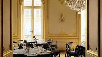 Ein formeller Speisesaal mit einem großen Tisch, der für eine Mahlzeit gedeckt ist, verzierten Wanddekorationen und einer Kristallleuchter.